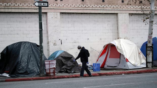 FILE - In this March 20, 2020, file photo, a man covers his face with a mask as he walks past tents on skid row in Los Angeles. The 9th U.S. Court of Appeals on Thursday, Sept. 23, 2021, overturned a federal judge’s sweeping order that required the city and county of Los Angeles to quickly find shelter for all homeless people living on downtown’s Skid Row. (AP Photo/Marcio Jose Sanchez, File)