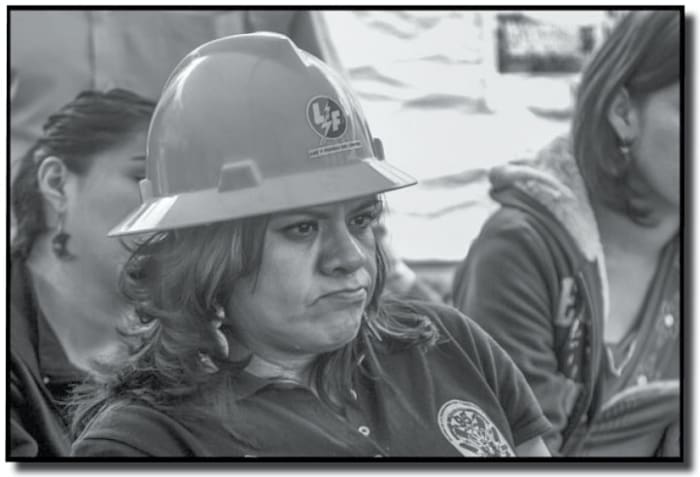 Elva Nora Cruz is the sister of a fired member of the Sindicato Mexicano de Electricistas (SME). 44,000 workers were fired and the state-owned electrical company was dissolved as part of the wave of privatization and economic reforms in the wake of NAFTA. She sits with Triqui women protesting violence in Oaxaca under a tent in Mexico City's central square, the zocalo (David Bacon, Stanford University Green Library)