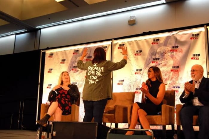 Ana Navarro shows off her jacket with a fashion statement spoofing Melania Trump. On the left of Navarro is moderator Virginia Heffernan and to her right are Amanda Carpenter and Trump biographer Michael D’Antonio.