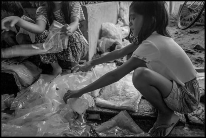 A girl in the Compostela Valley flattens plastic sheets coated with Lorsban. Photo copyright © 2020 by David Bacon.