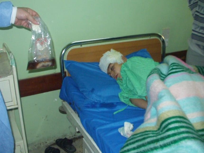 In Baghdad, 2003, 8 year old Mueen survived a U.S. aerial attack which killed his father. In the bag are part of his intestines. (Photo credit: Cathy Breen)