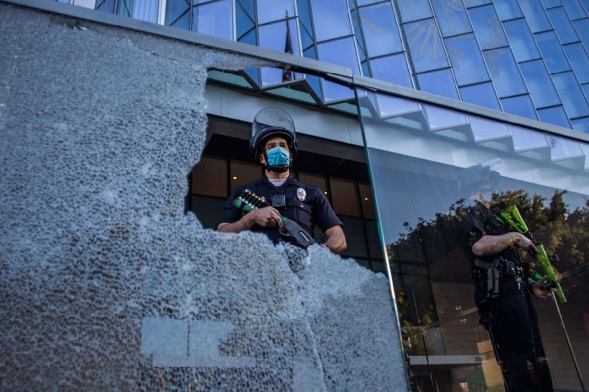 A police officer is seen through a broken glass at the U.S. Courthouse in Downtown Los Angeles, California, on July 25, 2020. (Apu Gomes/AFP)