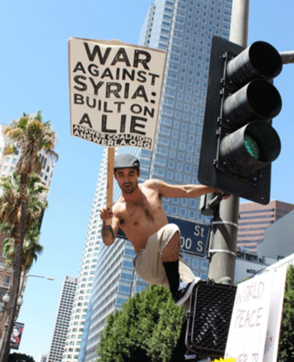 Ruben Ramirez Jr. climbs a lamp post outside Pershing Square. Ramirez said he joined the protest for his brother who is in the military. (Dan Bluemel / LA Activist)
