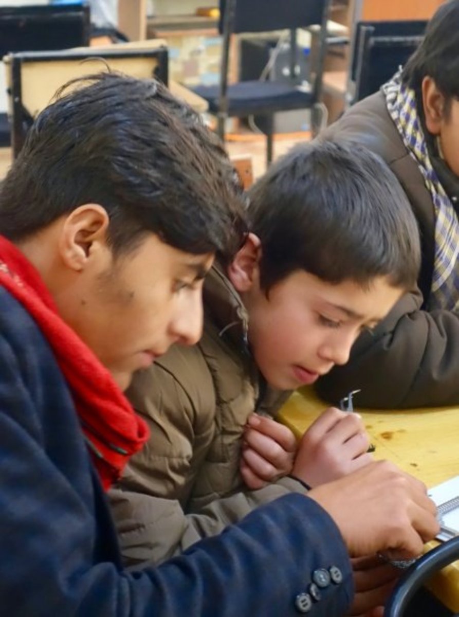 Saabir Gulmadin, left, works with a fellow Street Kids School student during a cell phone repair course at Gharejestan University.