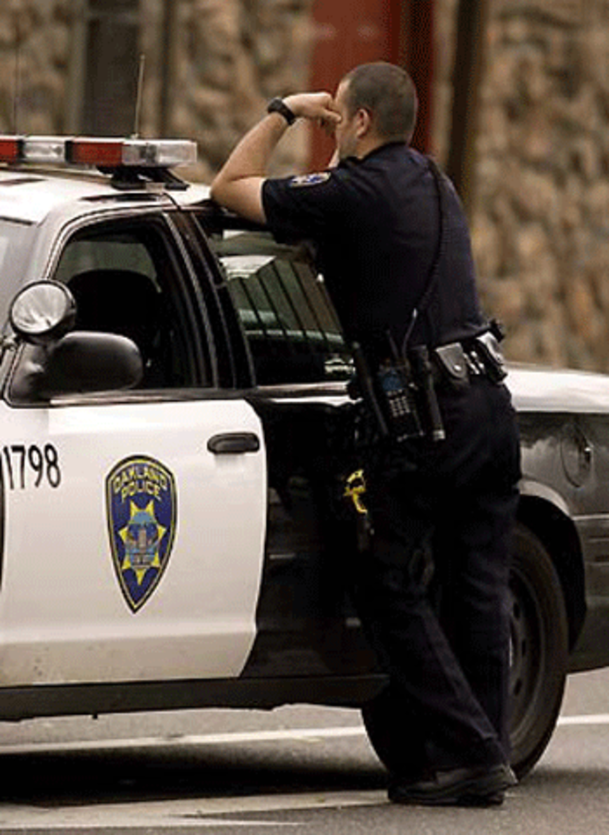 An Oakland police officer pauses by his patrol car near the scene of a police involved shooting on MacArthur Boulevard where two police officers were shot, Saturday, March 21, 2009 in Oakland, Calif.(Xinhua/AP Photo)