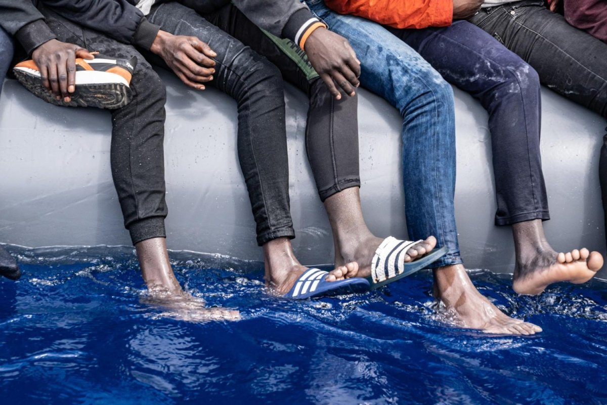 Men on a smuggler's boat in the Mediterranean Sea straddle the inflatable sides as there isn’t enough room for everyone to sit. May 10, 2022. Photo by Lexie Harrison-Cripps for palabra